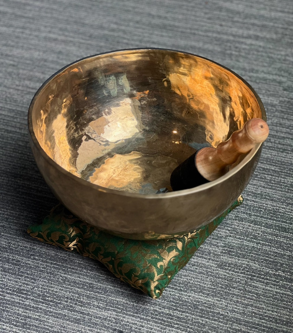 A golden singing bowl with a wooden mallet resting on a green and gold pillow.