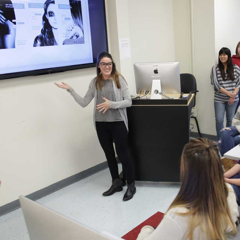 Graphic design student presents in front of a video screen in a UMass Lowell classroom