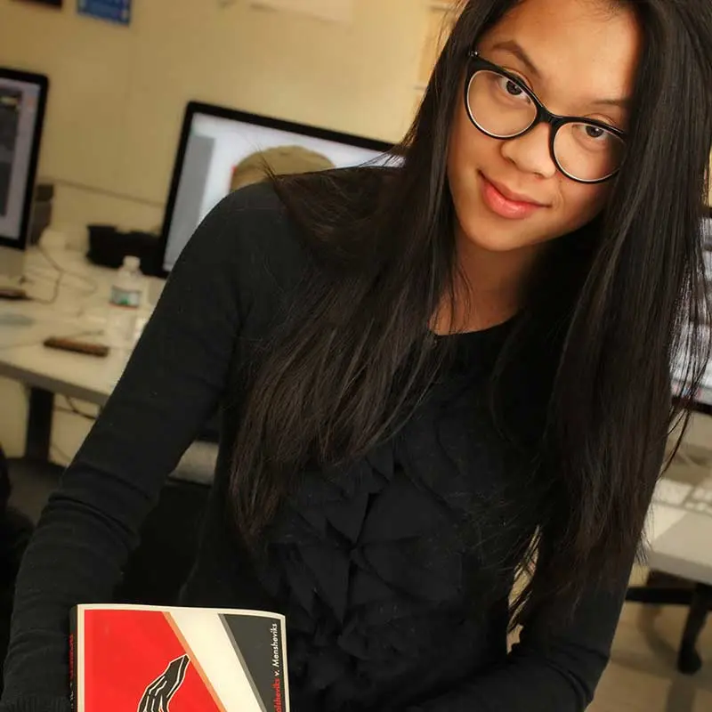 Graphic design student holds a book cover design in a UMass Lowell classroom