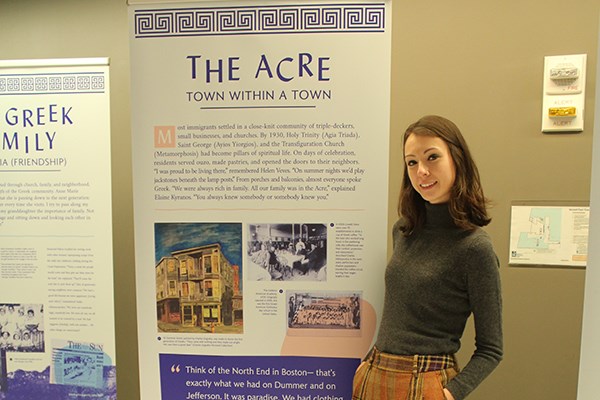 UMass Lowell honors history major Sophie Combs posed by first panel of exhibit on Greek immigration to Lowell