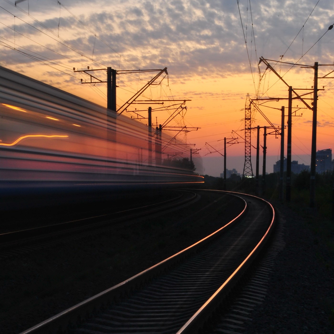 A train speeds past rows of electricity pylons at sunset.