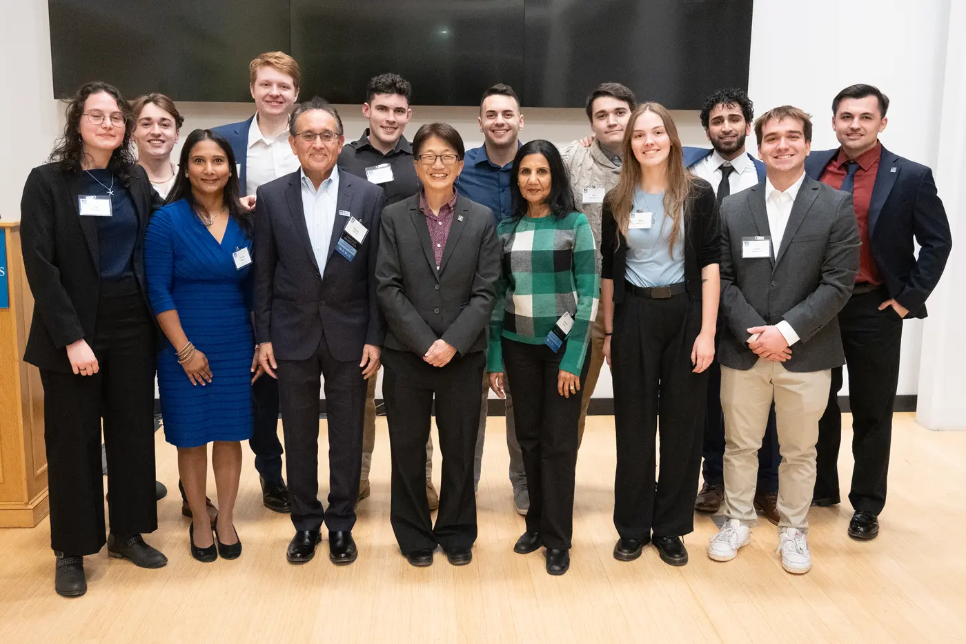 14 students and university staff members pose for a group photo in a room.
