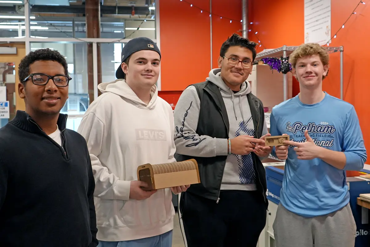 Four students hold up a toy made for a guinea pig.