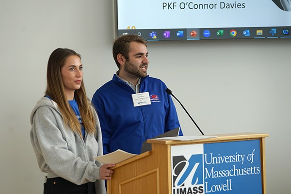 A young woman and man speak while standing at a podium