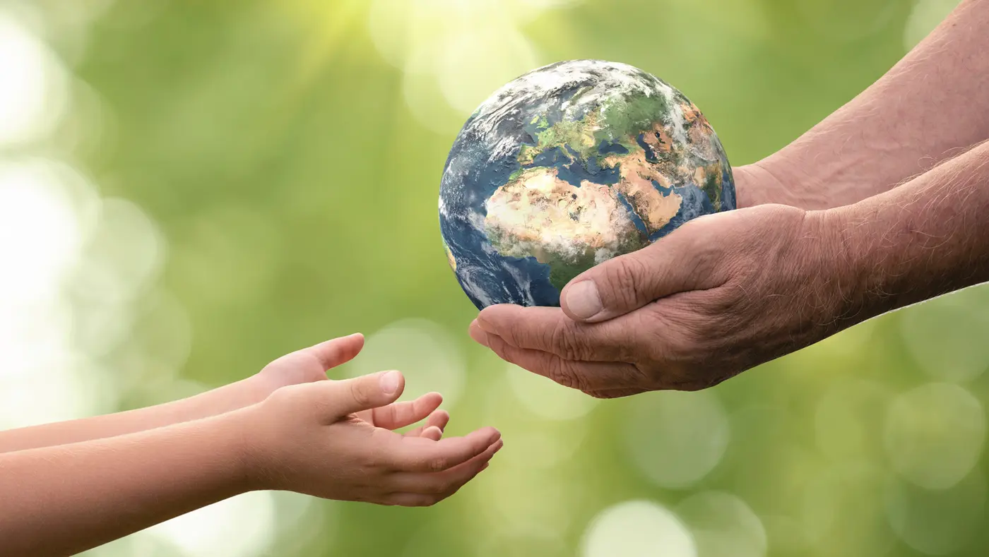 Close up of senior hands giving a model planet earth to a child with forest & sunlight in the background