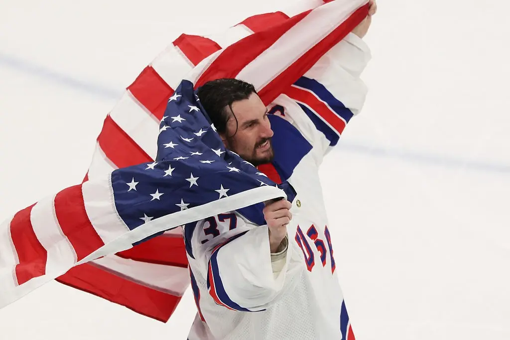 Team USA goalie Connor Hellebuyck skates draped in the U.S. flag.