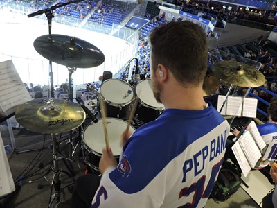 The image is of the drum set player looking down at the rest of the hockey pep band at the Tsongas Center where the band performs at all home hockey games. Selecting this link will take you to the home page for the hockey pep band with details to join and dates of performances.
