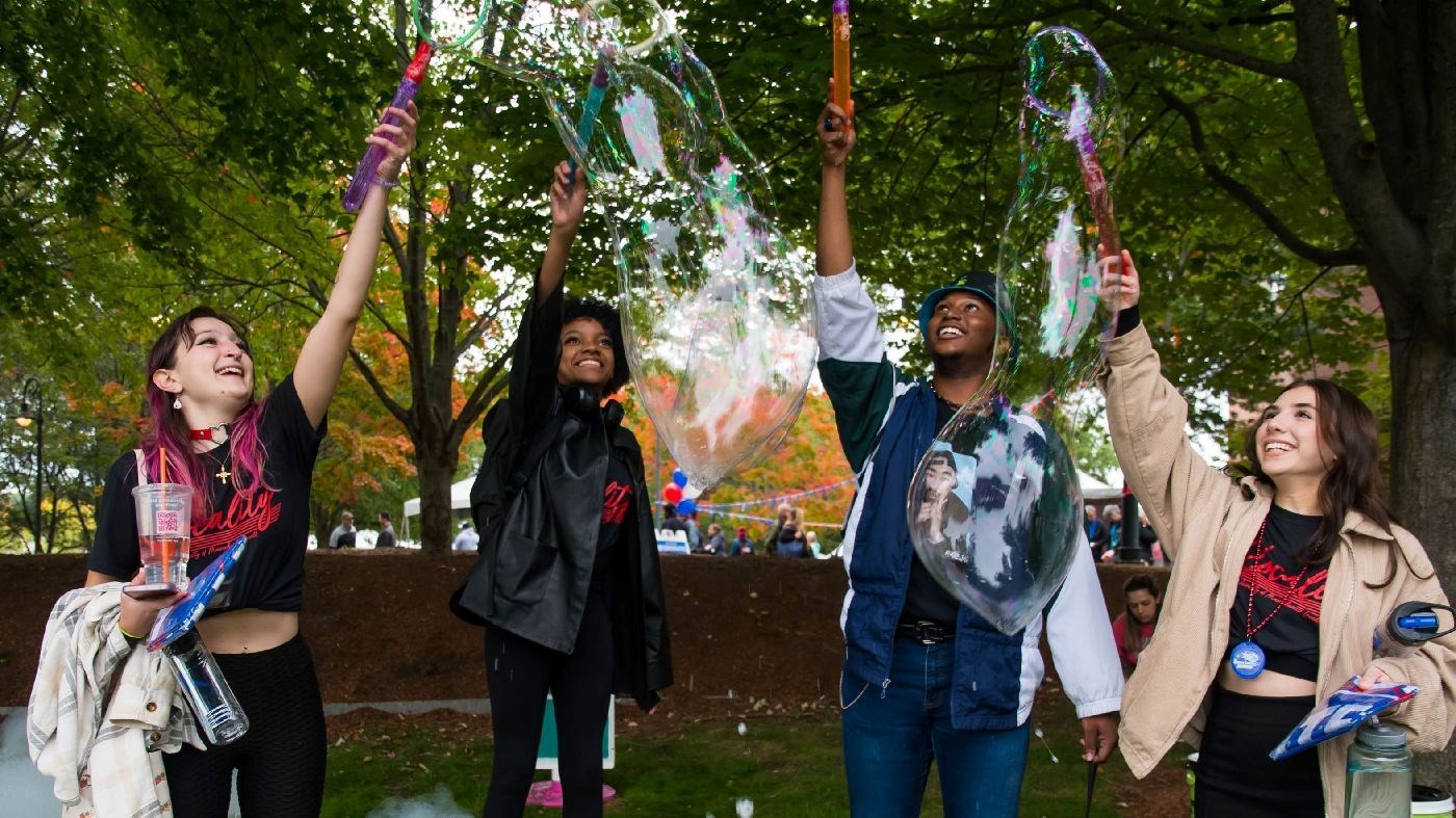 Four students blow bubbles with wands outside