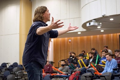 A man gestures with his hands to students in an auditorium