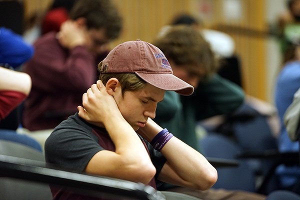 A student in baseball cap holds the back of his neck with his hands and stretches