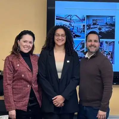 Three people stand in front of a digital display screen.