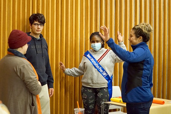 A woman wearing a face mask and a sash takes part in an exercise with three other people