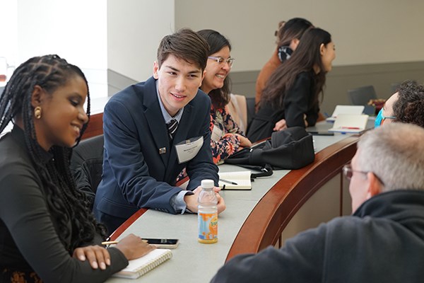 A half-dozen smile students talk at a long desk