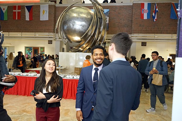 Two men in suits and a woman talk in front of a statue of a globe