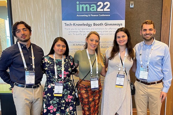 Five students - three women and two men - pose for a photo in front of an IMA 2022 sign