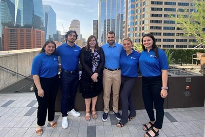 Five students in blue polo shirts pose with a woman in a roof in downtown Austin