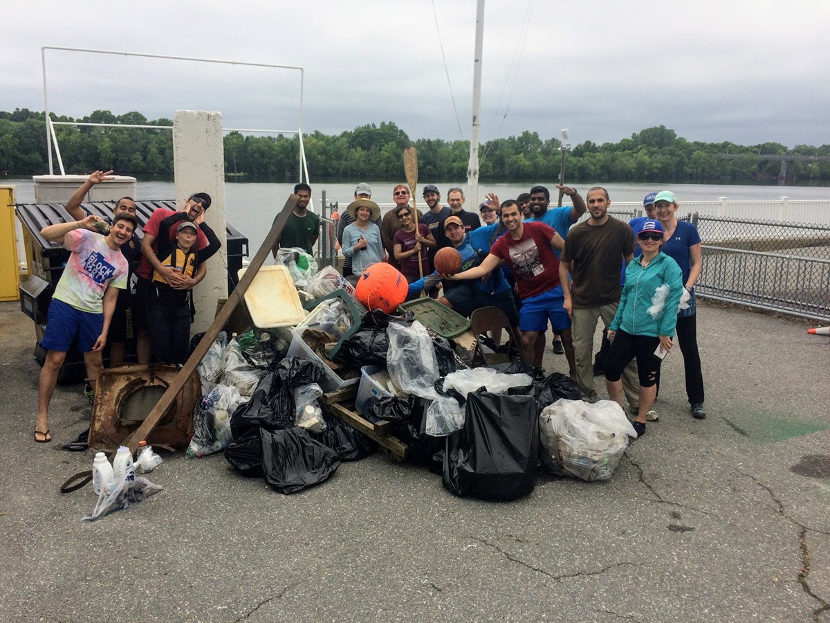 Proud group of people gathered around a large pile of debris they removed from the river bank.