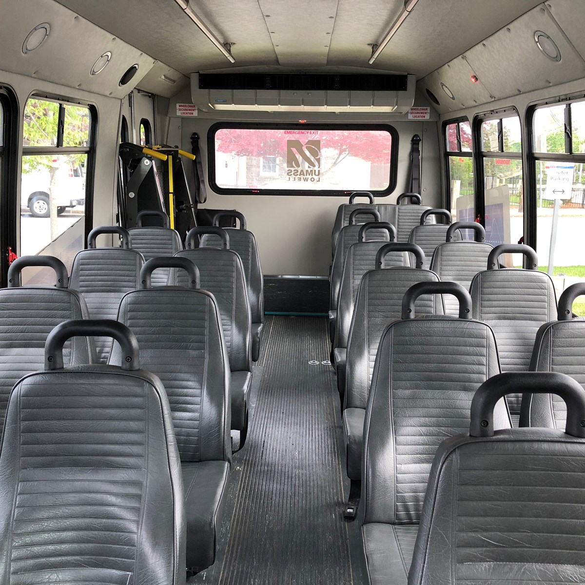 The interior of a 20 passenger shuttle bus with grey seats, and a light grey ceiling. There is a wheelchair lift in the rear. 