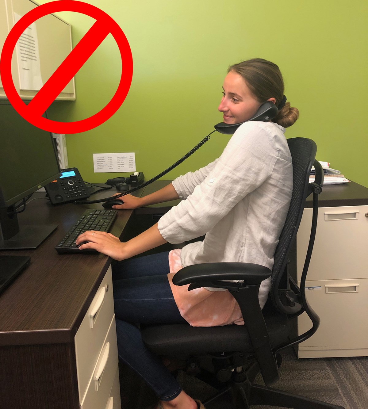 A no sign over an image of a woman sitting at her desk while using the phone. The phone is being held between her shoulder and ear.
