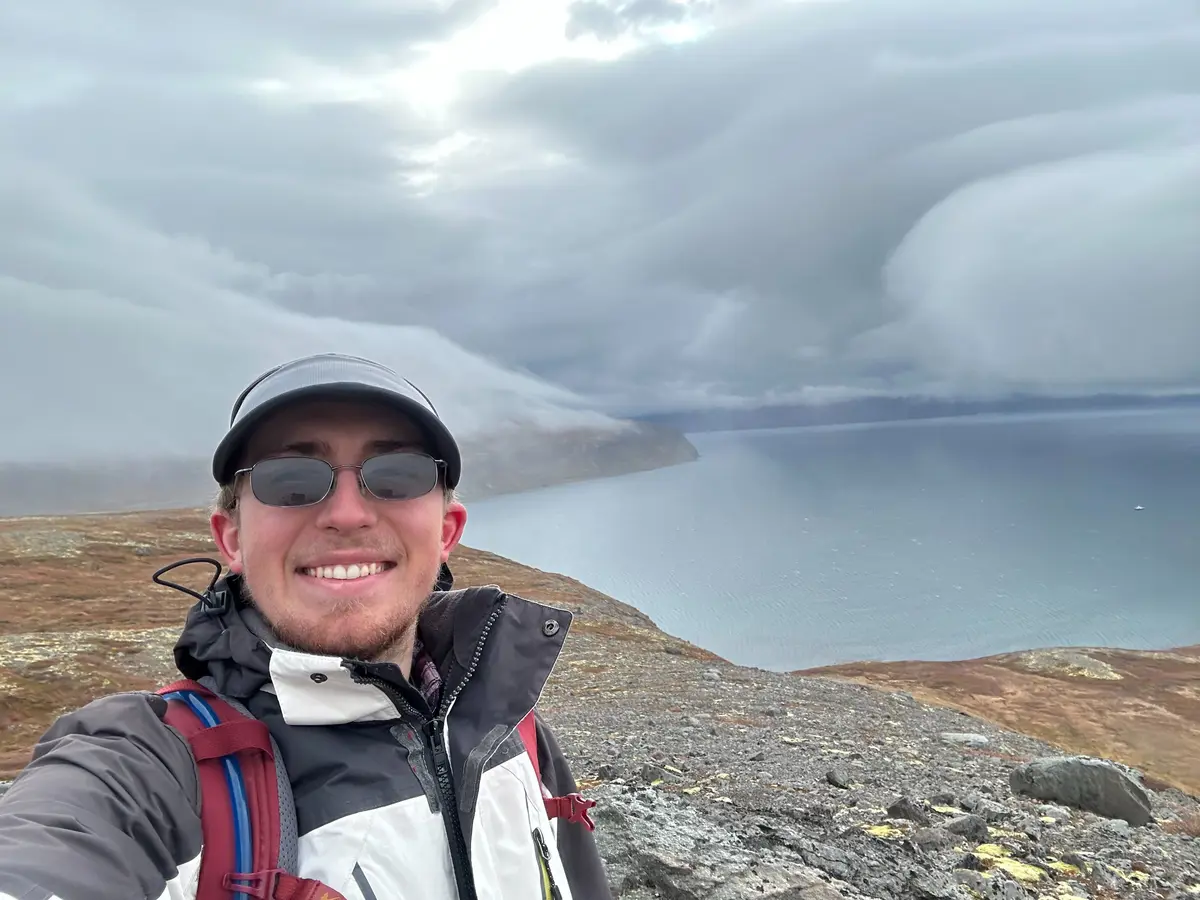 A young man takes a selfie in front of a body of water.