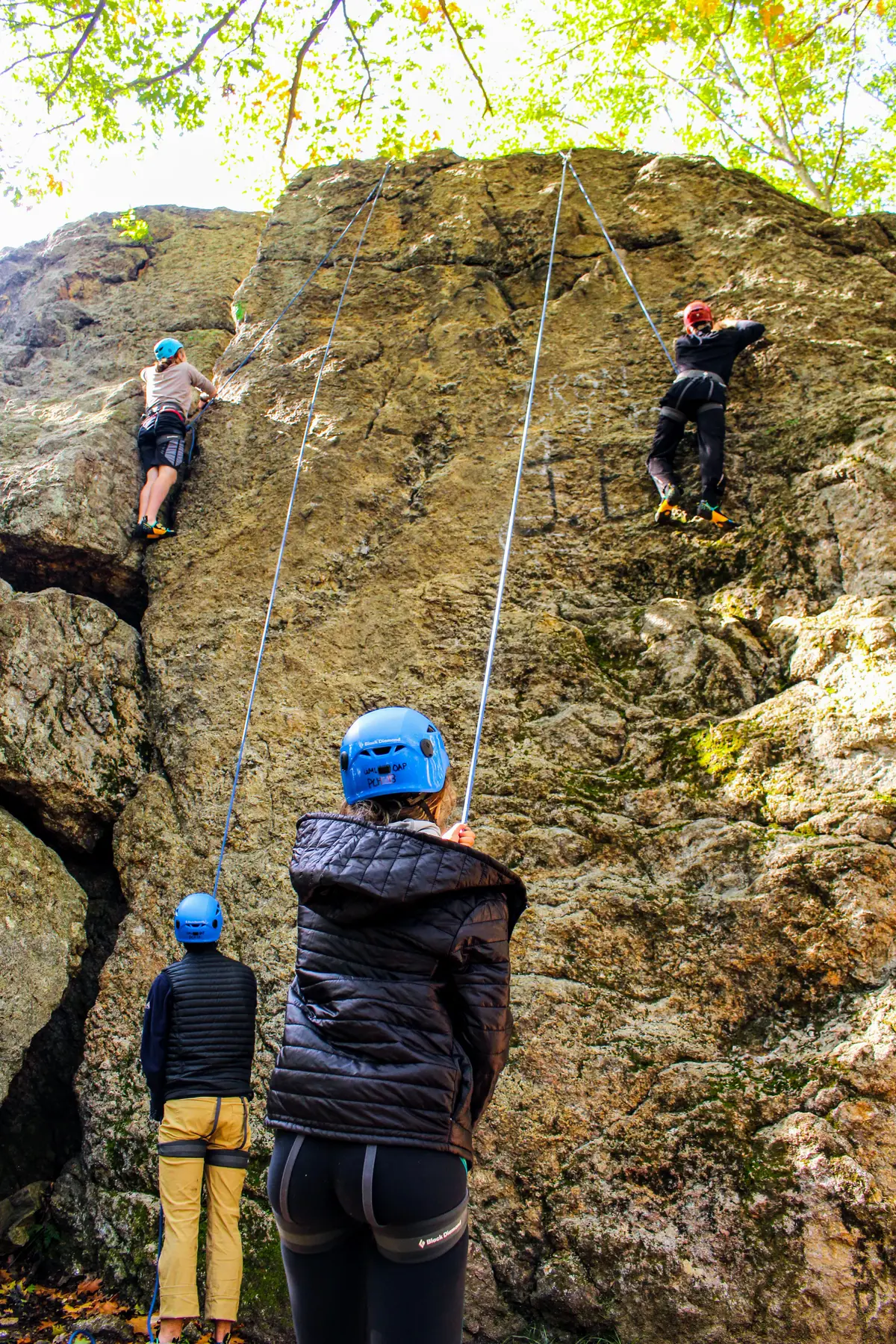 Rock Climbing at Den Rock Lawrence - Two climbers on a cliff and belayers below