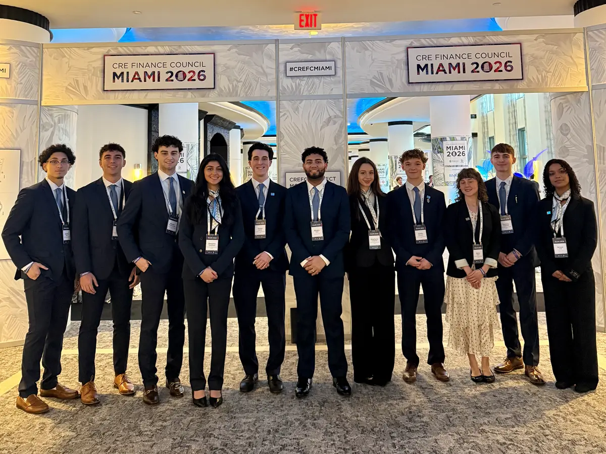 Eleven college students in business outfits pose for a photo at a convention.