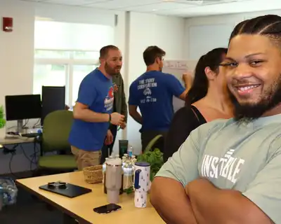 Student smiling and looking at the camera, with other students gathered in the background.