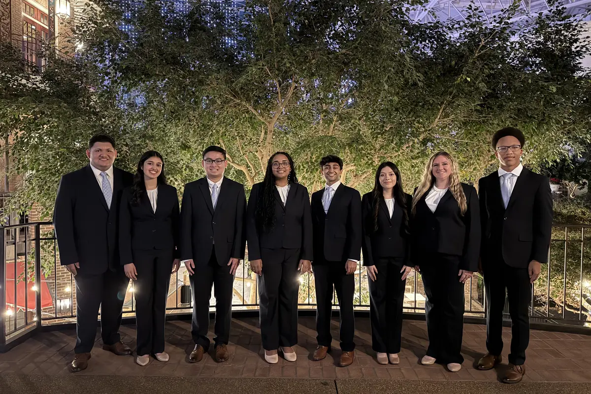 Eight young men and women in business attire pose for a photo in front of a tree.