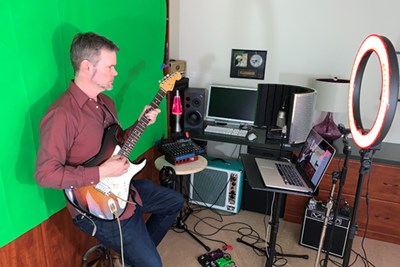 The music faculty faces unique challenges in moving classes and rehearsals online. Prof. John Shirley has organized a virtual teaching station in his home. During class, he flashes familiar campus scenes on the green screen behind him.