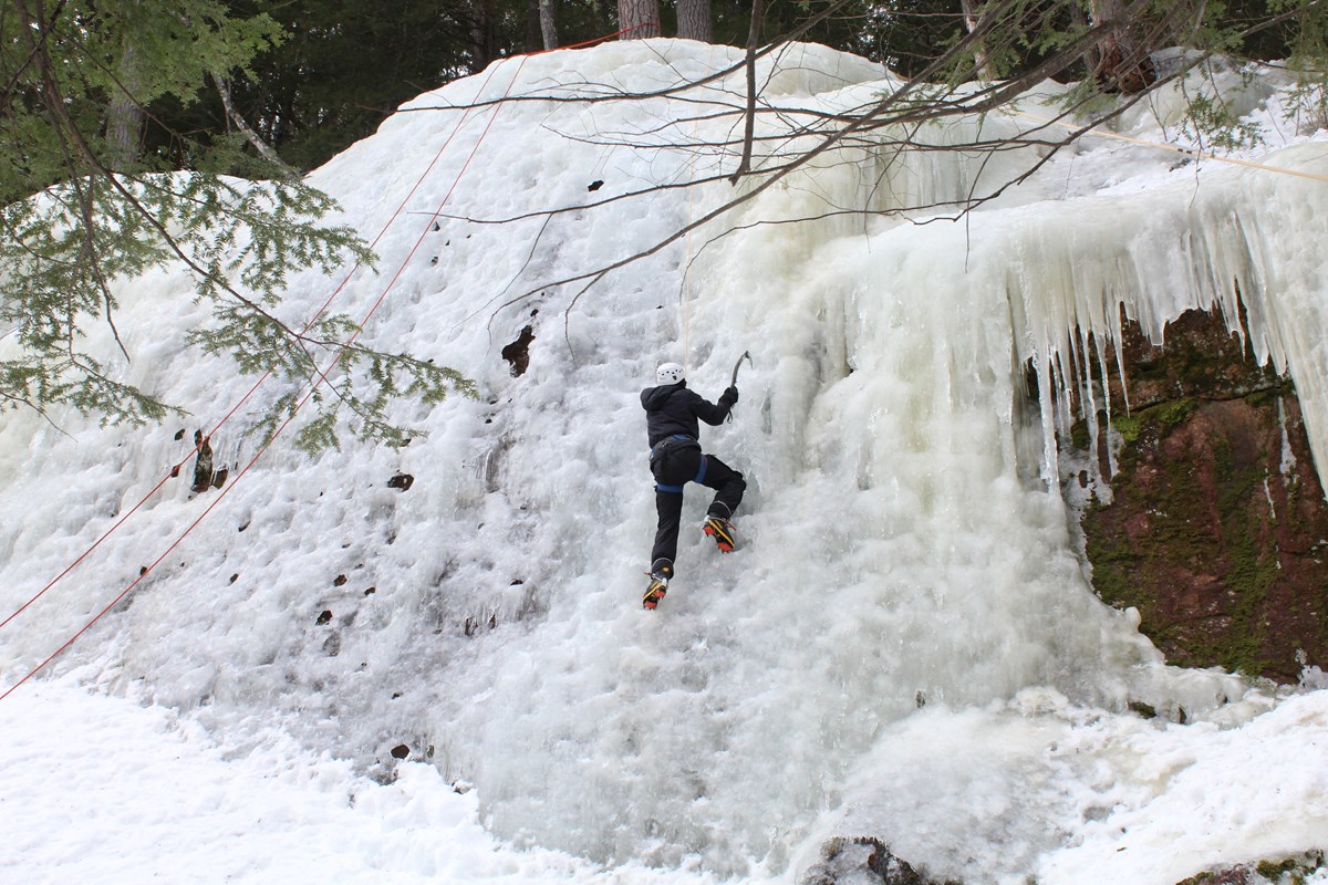 One person climbs on a large wall of solid ice.