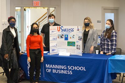 Five students, four women and a man, pose for a photo with their USuccess project board