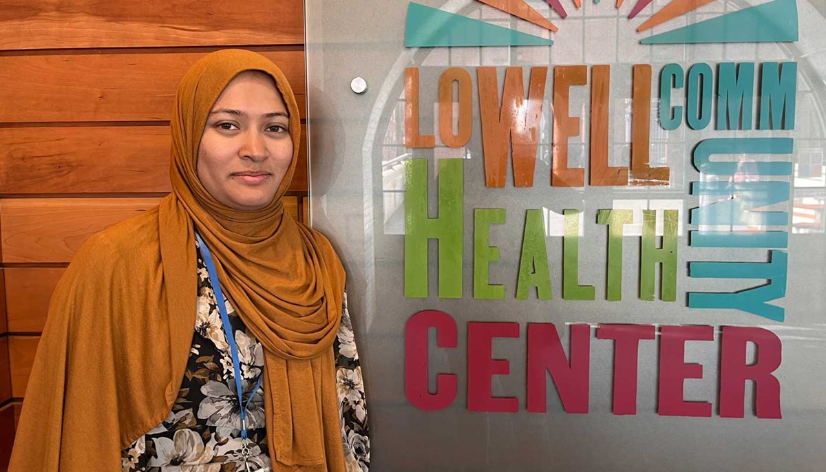 UMass Lowell student Iffat Farah poses next to a sign for the Lowell Community Health Center.