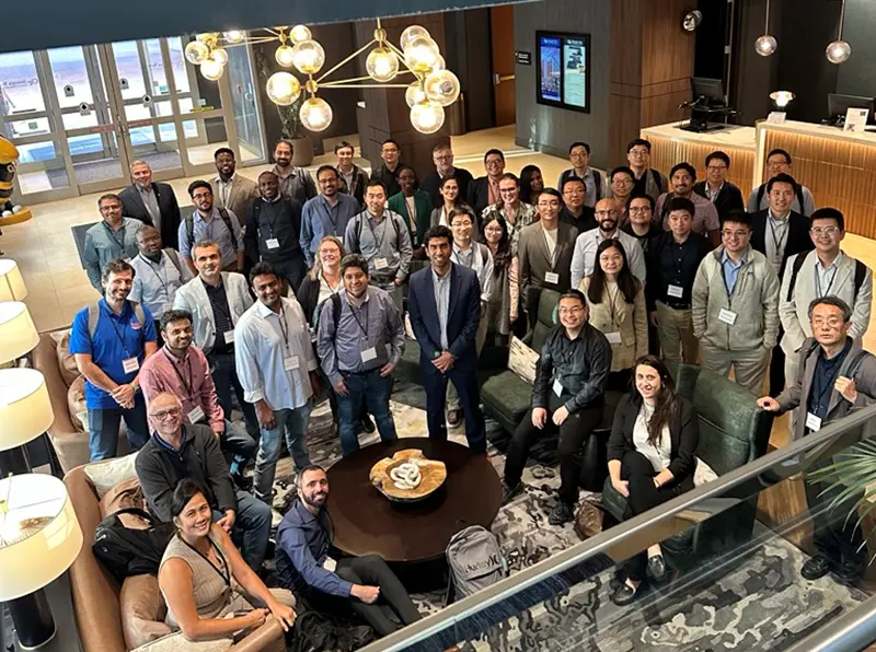 Nripojyoti Biswas posing in a group photo with conference attendees in a hotel lobby.