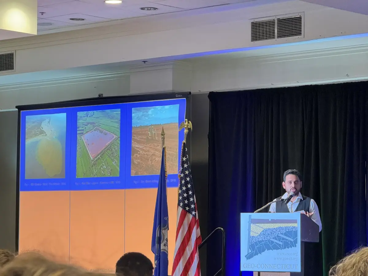 João Machado presenting his research on a podium with slides at a conference.