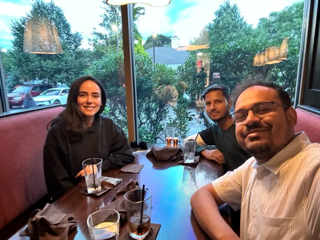 Nripojyoti Biswas and 2 UMass Lowell students sitting at a restaurant table and smiling.
