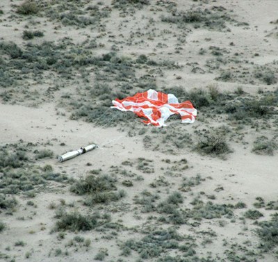 Imager II is lying in a field of grass and sand. The cylindrical capsule is attached to a parachute.