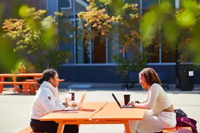 Two students seated outdoors at a picnic table.