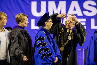 A man places a medal around a woman's neck while wearing academic regalia