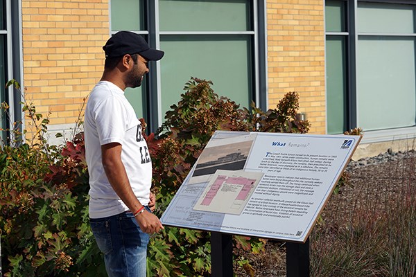 A student in a baseball cap reads a sign about Indigenous peoples outside