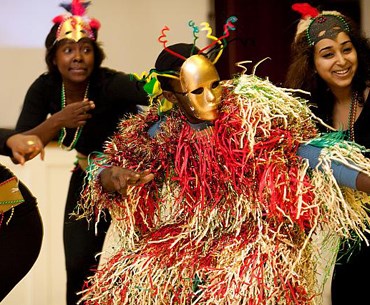 A group of students participating in the international festival, dancing and wearing traditional mask and clothing from their culture. 