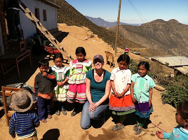 UMass Lowell Female student wearing a Boston Red Sox baseball posting for a picture with a number of children while in Peru.