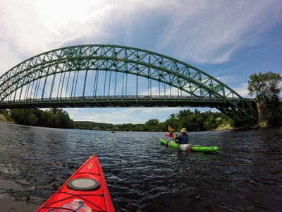 Kayakers approaching under a large green arch bridge.