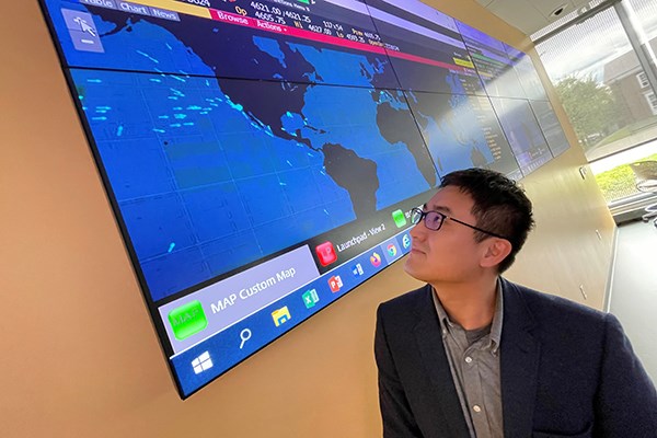 A man in glasses looks up at a large monitor showing a map of the United States