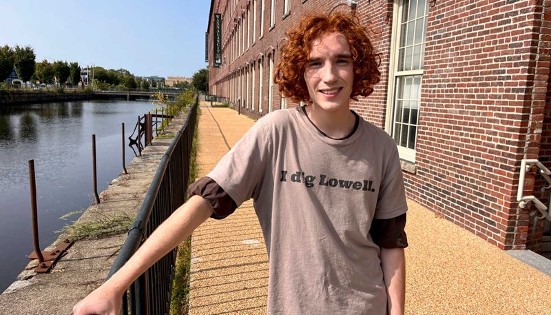 UMass Lowell student Jack Callahan stands outside along a canal and brick building in Lowell. 
