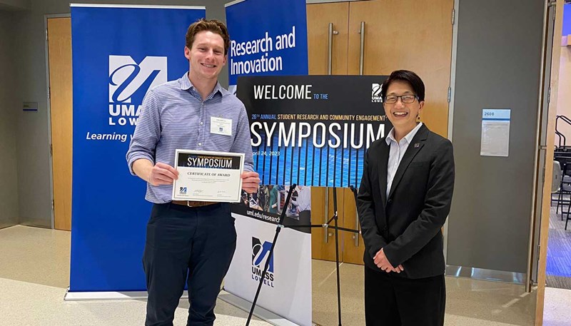Jamie Aciukewicz stands with UMass Lowell Chancellor Julie Chen in front of banner for the 2023 Student Research and Community Engagement Symposium.