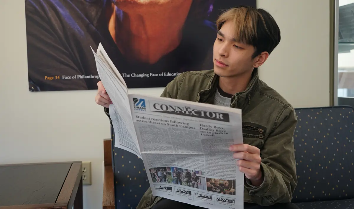 Jesse Nguyen sitting down reading the UML Connector newspaper.
