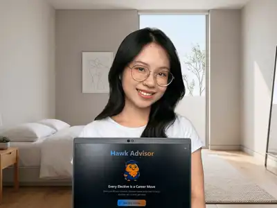 A young woman with dark hair and round glasses poses for a photo with a laptop in a bedroom.