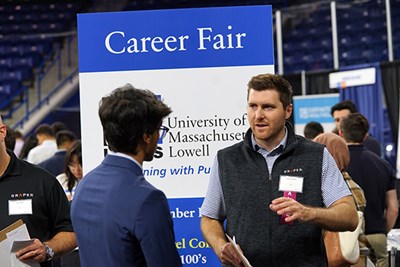 A man in a vest talks to a student at a career fair