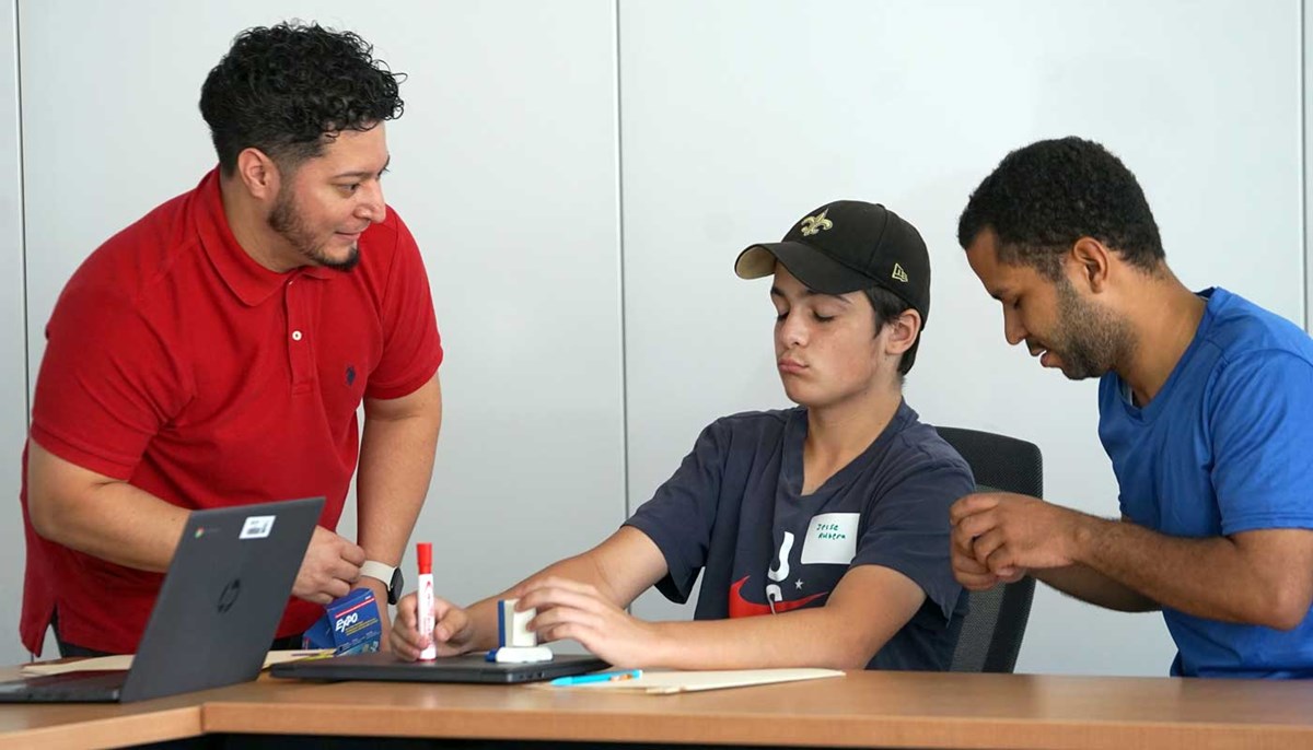 Jonathan Aguilar talking with two students at a desk