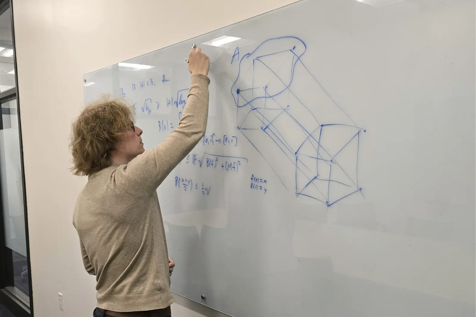 A person in a tan shirt writes on a dry erase board in a college classroom.